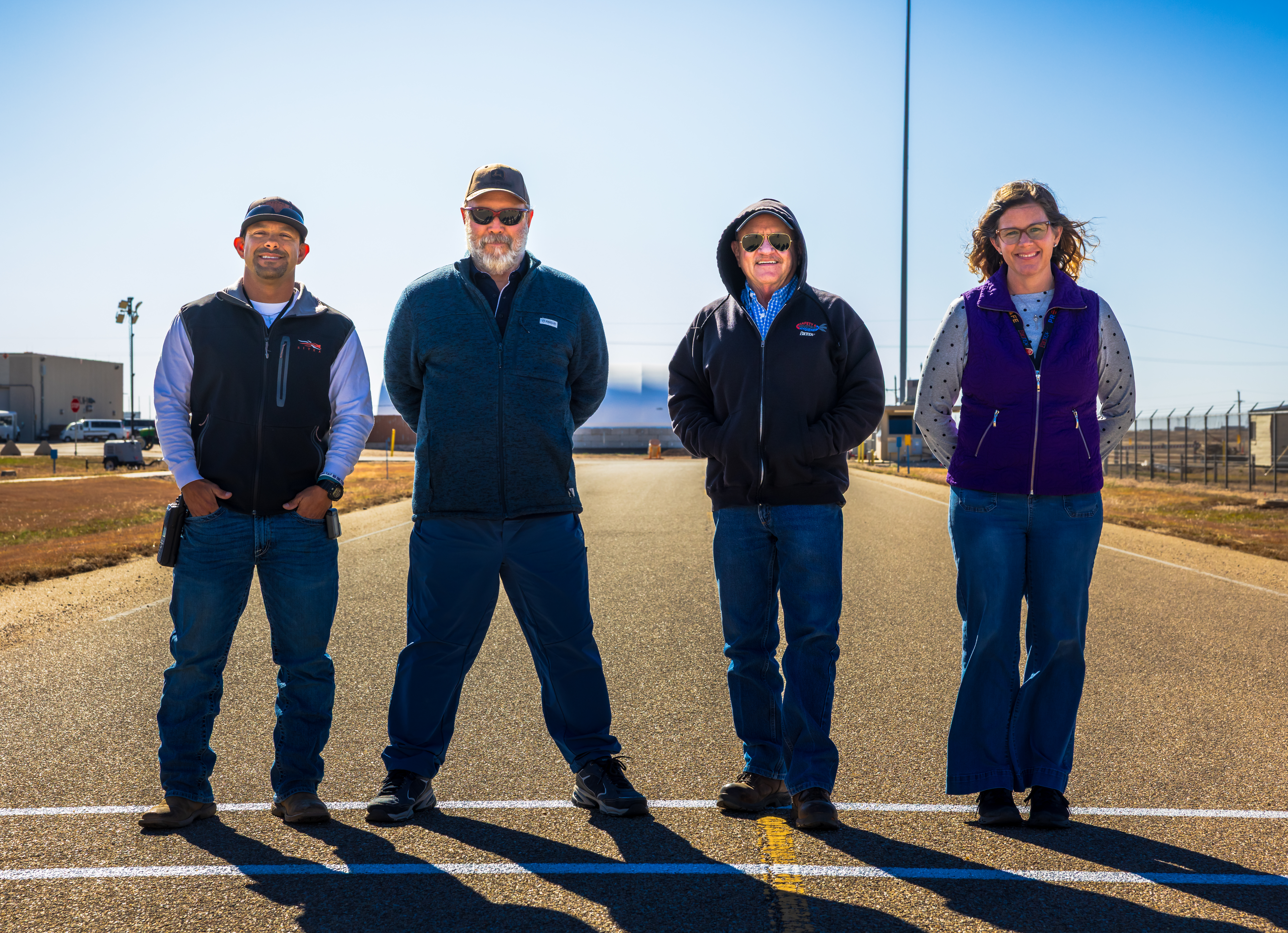 Members of the SWAT team stand in the newly painted walking path leading from the Building 16-37 Argus to Building 16-001 Three men and one woman stand in the middle of a roadway on a walking path, facing the camera and smiling.